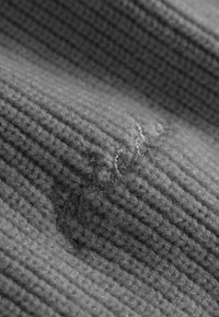 Wollen kledingstuk met een textuur in verschillende grijstinten, voorzien van een subtiele geborduurde detail in een contrasterende kleur.