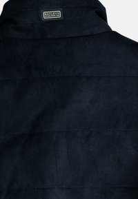 Marineblauer, gestepptes Stoff-Weste mit subtiler Textur, verfügt über einen Kragen und ein rechteckiges Etikett, das auf der Rückseite genäht ist.