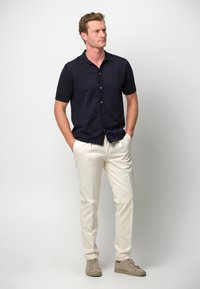 Camicia a maniche corte blu navy con bottoni, pantaloni bianchi e sneakers beige; vestibilità casual, tessuto morbido e design minimalista.