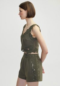 Completo a due pezzi verde oliva con dettagli in pizzo intricato lungo i bordi e pantaloni corti coordinati, caratterizzato da pietre decorative sulla cucitura laterale.