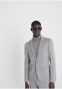 Chaqueta de traje gris claro con cierre de un botón, solapas con muesca y un bolsillo en el pecho, combinada con un cuello de tortuga acanalado en un tono a juego.