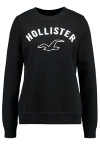 Černá mikina vyrobená z bavlny, s kulatým výstřihem, dlouhými rukávy a bílým logem "HOLLISTER" s grafikou ptáka na hrudi.