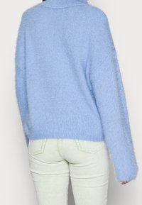 Ljusblå, fluffig tröja med hög krage och nedfallna axlar, matchad med ljusgröna, ribbade jeans. Mjuk textur och avslappnad passform.