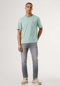 Camiseta a rayas en verde menta con rayas blancas y rosas, de manga corta, cuello redondo, con un pequeño logo en el lado izquierdo del pecho.