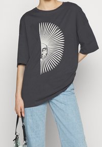 Tmavě šedé oversized tričko s bílou grafikou slunce a měsíce. Měkká bavlněná tkanina s krátkými rukávy a volným střihem.