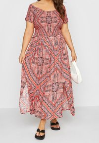 Maxiklänning i röd och svart paisleymönster, med off-shoulder halslinje, korta ärmar och flödande design. Matchad med svarta sandaler.