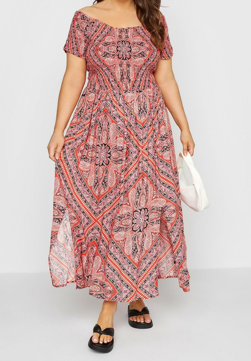 Maxiklänning i röd och svart paisleymönster, med off-shoulder halslinje, korta ärmar och flödande design. Matchad med svarta sandaler.