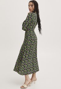 Abito midi floreale caratterizzato da uno sfondo scuro con motivi di fiori verdi e viola, maniche lunghe, vita aderente e un orlo fluido.