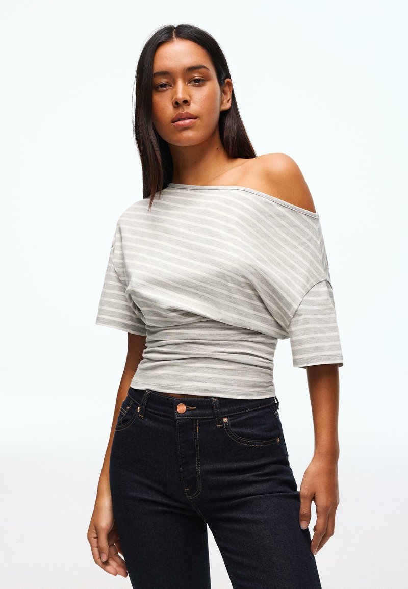 Sivi in beli črtasti zgornji del z odprtimi rameni in kratkimi rokavi, kombiniran s temno modrimi kavbojkami z oranžnim šivom in sprednjimi žepi.