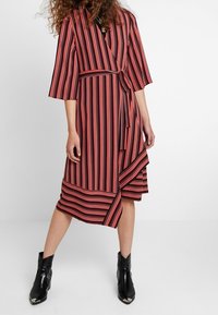 Robe portefeuille à rayures rouges et noires, manches trois-quarts, ourlet asymétrique et taille ceinturée. Conçue dans un tissu lisse et léger.