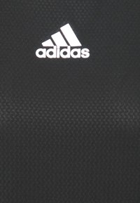 Svart atletisk klädsel med en texturerad tyg, med en framträdande vit Adidas-logotyp centrerad högst upp.