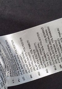 Etykieta z informacjami o składzie materiału w kilku językach, podająca 70% poliester i 30% bawełny na produkcie tekstylnym.