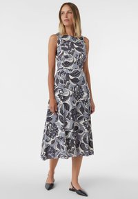 Ärmelloses Midikleid in Hellblau mit floralem Muster in Dunkelblau und Weiß. Der Stoff hat eine glatte Textur. Schwarze spitze Ballerinas.