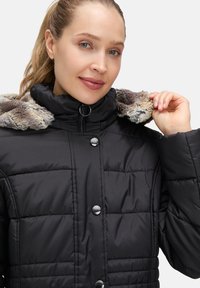 Czarna kurtka puchowa z zamkiem błyskawicznym, zatrzaskami i kołnierzem wyłożonym futrem. Materiał jest gładki, z pikowanymi sekcjami dla lepszej izolacji.