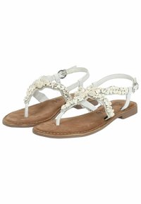 Sandales blanches avec un design tressé, ornées de petites coquilles décoratives, dotées d'une semelle plate et d'une bride de cheville. Semelle en faux suède.