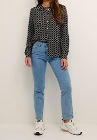 Svartvit mönstrad skjorta med knappar, blå högmidjade jeans och vita sneakers med svarta detaljer. Slätt tyg, avslappnad passform.