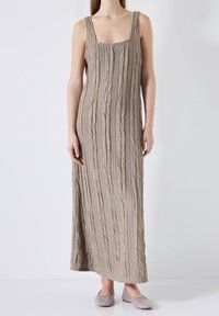 Robe longue beige sans manches avec un design texturé et froissé. Bretelles lisses et décolleté carré. Associée à des chaussures plates scintillantes.