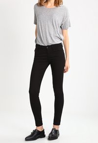 Svarta smala jeans i kombination med en grå kortärmad t-shirt. Jeansarna har en enkel design och en slät, mjuk textur. Svarta läderskor fulländar looken.