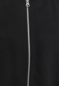 Indumento lavorato a maglia nero con una cerniera argento che scorre lungo il centro. La trama appare liscia con un motivo uniforme.
