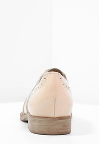 Chaussure en cuir beige clair avec une texture lisse, ornée de perforations décoratives, un bout arrondi et un petit talon en bois.