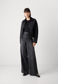 Černá prošívaná bunda s límcem, spárovaná s trendy tmavými džíny s vysokým pasem. Tkanina je hladká s jemným vzhledem; elegantní obuv dokončuje vzhled.
