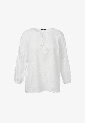 Witte blouse met een ronde halslijn, lange mouwen en textuurpatronen van harten verspreid over de stof. Heeft een strikdetail bij de hals.