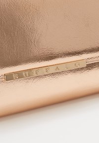 Superficie de cuero texturizado en oro rosado metálico con una pequeña placa de metal dorado grabada con la palabra "BUFFALO."