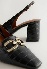Mustat, krokotiilikuosiset slingback-kengät, joissa on terävä nenä ja kultaiset yksityiskohdat; teksturoitu materiaali ja kömpelö, neliömäinen korko.