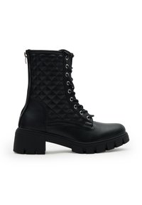 Botas de combate de cuero negro con paneles laterales acolchados, parte delantera con cordones, suela gruesa y cierre de cremallera en la parte trasera, mostradas en perfil lateral.