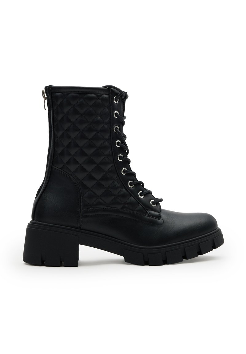 Botas de combate de cuero negro con paneles laterales acolchados, parte delantera con cordones, suela gruesa y cierre de cremallera en la parte trasera, mostradas en perfil lateral.