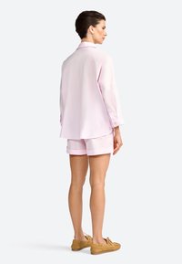 Light pink oversized shirt with long sleeves and a rounded hem, paired with matching shorts. The model wears brown boat shoes.