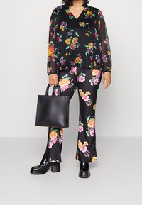 Luftigt sort bluse med levende blomsterprint, parret med matchende blomsterbukser. En sort lædertaske og kraftige sorte sko fuldender looket.