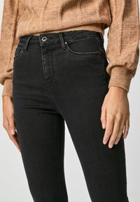 Jeans de mezclilla negra con un ajuste slim, que cuentan con un diseño tradicional de cinco bolsillos y un cierre de botón. La tela es suave con un ligero estiramiento.