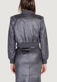 Cazadora bomber gris con una textura suave y lisa, puños acanalados y una cintura ajustada. Presenta costuras que crean una silueta estructurada.