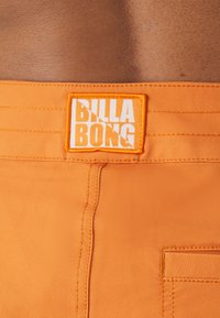 Shorts de bain orange avec un tissu texturé, des détails cousus et un patch logo BILLA BONG blanc et proéminent sur la taille.