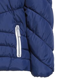 Sezione di giacca imbottita blu navy con motivo trapuntato diagonale, caratterizzata da una tasca con cerniera e dettagli in argento e una texture liscia.