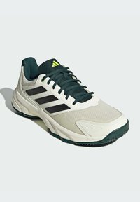 Chaussure de sport avec une tige en mesh léger et respirant en crème et vert foncé. Présente des rayures noires, des accents texturés et une semelle en caoutchouc.