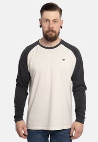 Long-sleeve raglan shirt features a cream body with dark gray sleeves. Notable bear graphic on the left chest. Soft cotton blend fabric.
