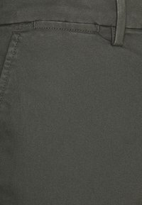 Tela de color gris oscuro con un patrón de tejido diagonal texturizado. Cuenta con lazos para cinturón y un bolsillo frontal, diseñado como parte de un pantalón.