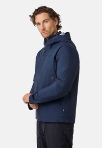 Giacca impermeabile blu navy con cappuccio, chiusura frontale con zip e tasche con zip. Presenta polsini regolabili e una texture liscia e leggera.