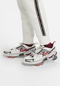 White athletic sneakers with black and red accents, textured mesh upper, visible air cushioning in the sole, and a dynamic pattern design.