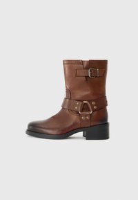 Bottine en cuir brun avec un bout rond, détail de boucle sur le côté et un petit talon carré. Fini lisse avec des accents métalliques contrastés.
