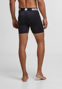Caleçons boxers noirs en tissu lisse, dotés d'une large ceinture élastique avec logo, et d'un design ajusté qui s'étend jusqu'au milieu de la cuisse.