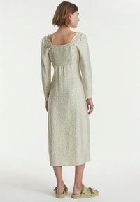 Midikleid aus hellgrünem Stoff mit weißen Polka-Dots, verfügt über einen quadratischen Ausschnitt, lange Ärmel und ein gerafftes Rückenteil.