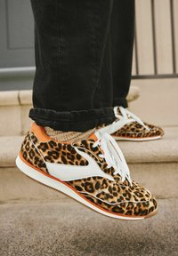 Sneaker im Leopardenmuster verfügen über eine Mischung aus braunen und schwarzen Texturen mit weißen und orangefarbenen Akzenten, weißen Schnürsenkeln und einer strukturierten Sohle.