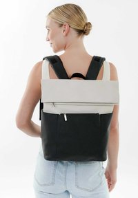 Mochila en materiales gris y negro con un diseño de tipo roll-top, que cuenta con correas ajustables y un bolsillo delantero con cremallera. Textura suave, aspecto moderno.
