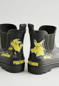 Bottes de pluie en caoutchouc noir avec des autocollants de Pikachu sur un fond jaune éclaboussé, présentant une tige texturée, des panneaux latéraux élastiques et des semelles robustes.