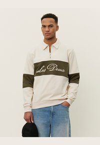Crème sweatshirt met een kwart-rits, olijfgroene band en wit "Les Deux" logo. Katoenmix, geribbelde manchetten en een relaxte pasvorm.