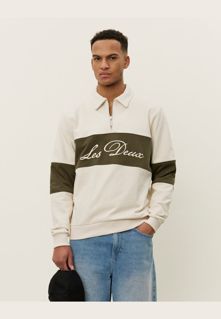 Crème sweatshirt met een kwart-rits, olijfgroene band en wit "Les Deux" logo. Katoenmix, geribbelde manchetten en een relaxte pasvorm.