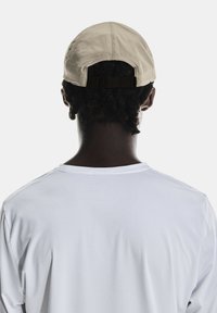 Cappello beige chiaro visto da dietro, caratterizzato da un tessuto testurizzato e una fascia regolabile, indossato con una semplice camicia bianca a maniche lunghe.